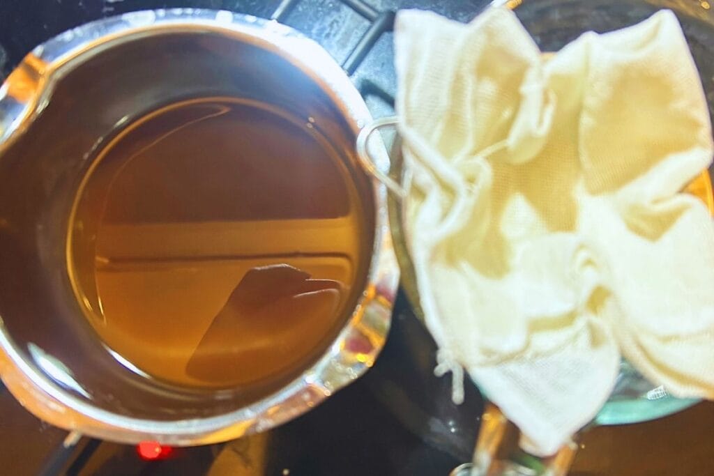 melted pumpkin spice lip balm mixture next to cheesecloth in sieve