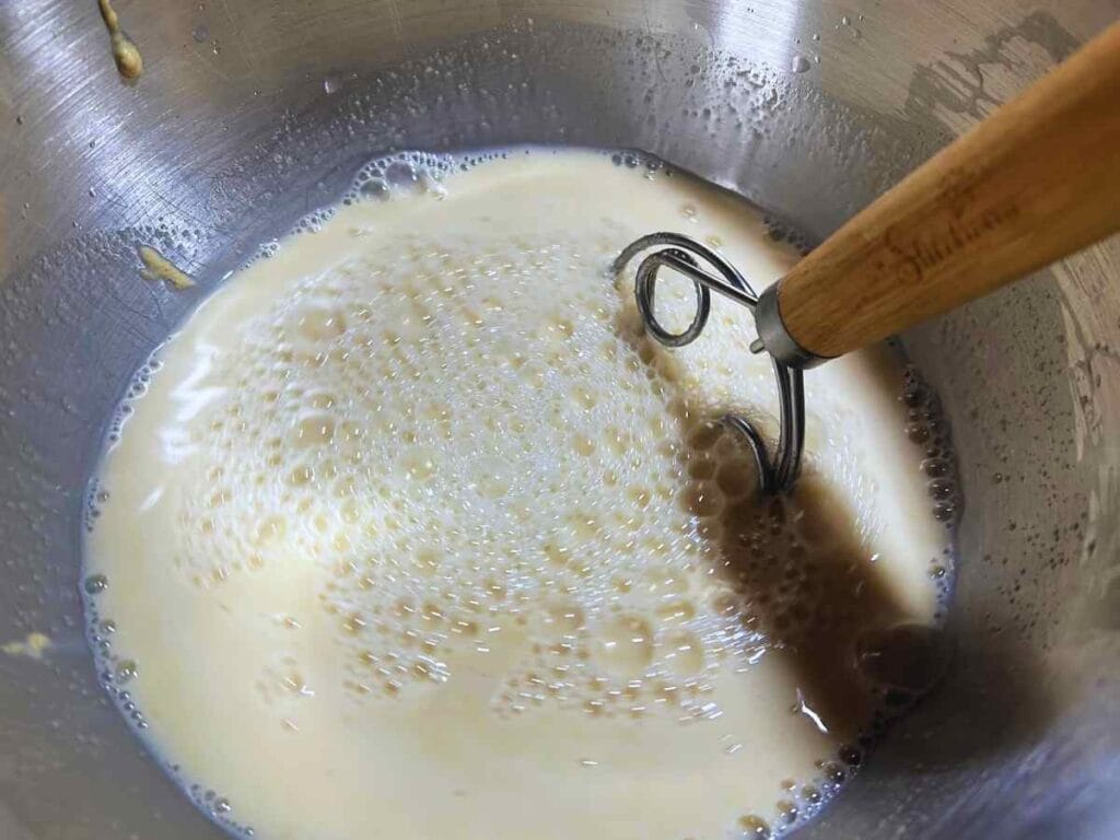 danish whisk mixing sourdough starter and water in a mixing bowl