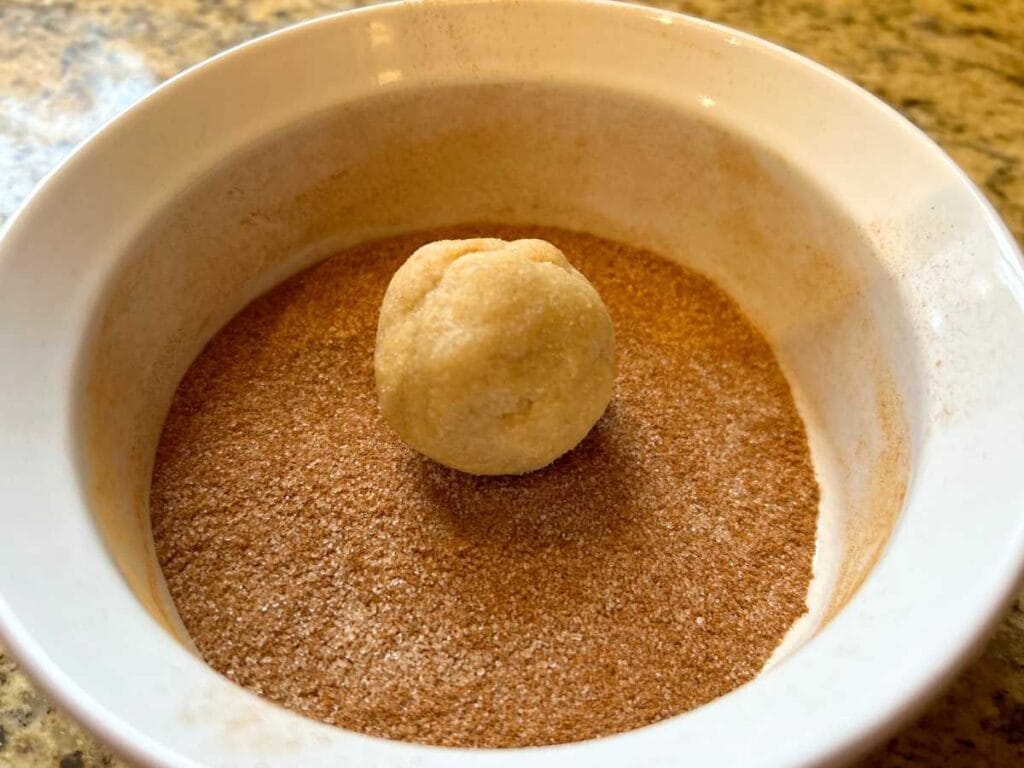 snickerdoodle dough ball in a ramekin of cinnamon sugar
