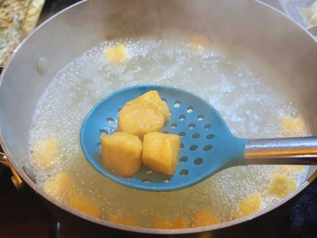 blue slotted spoon removing boiled pretzel bites from boiling water