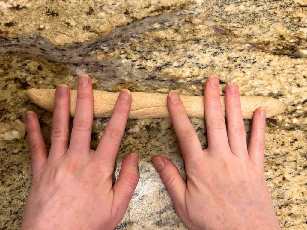 two hands rolling dough into log