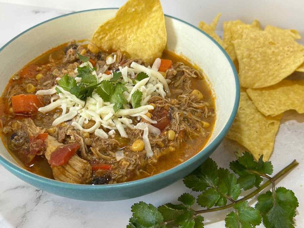 a bowl of Creamy Chicken Tortilla Soup topped with cheese and with chips and cilantro laid around it