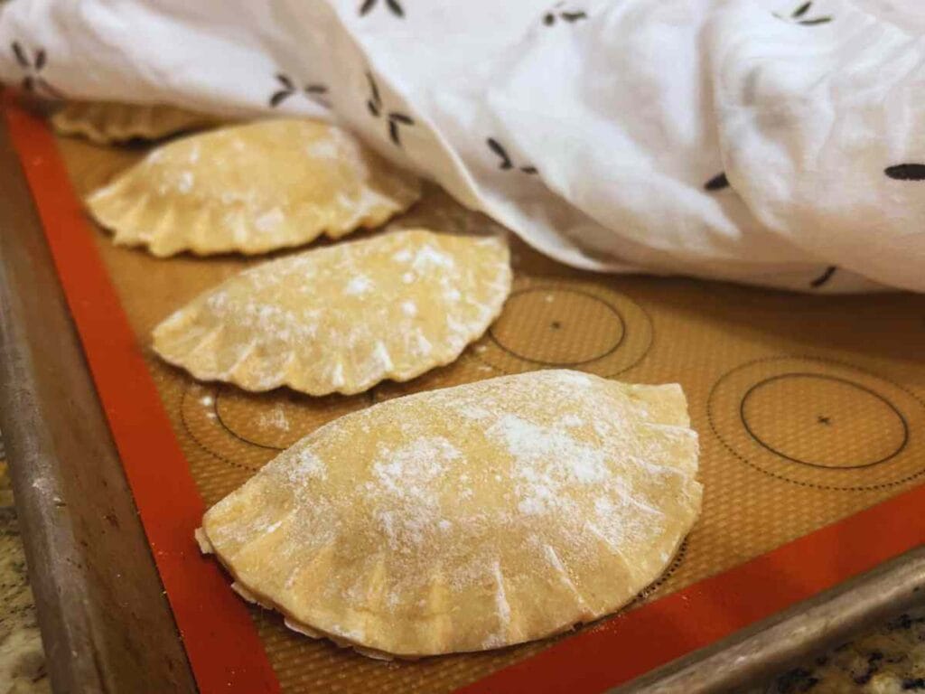 fresh made pierogies on a tray under a damp cloth