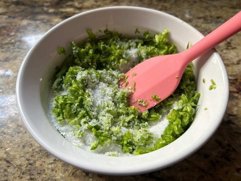 a pink spatula mixing together chopped greens and coarse sea salt in a ramekin