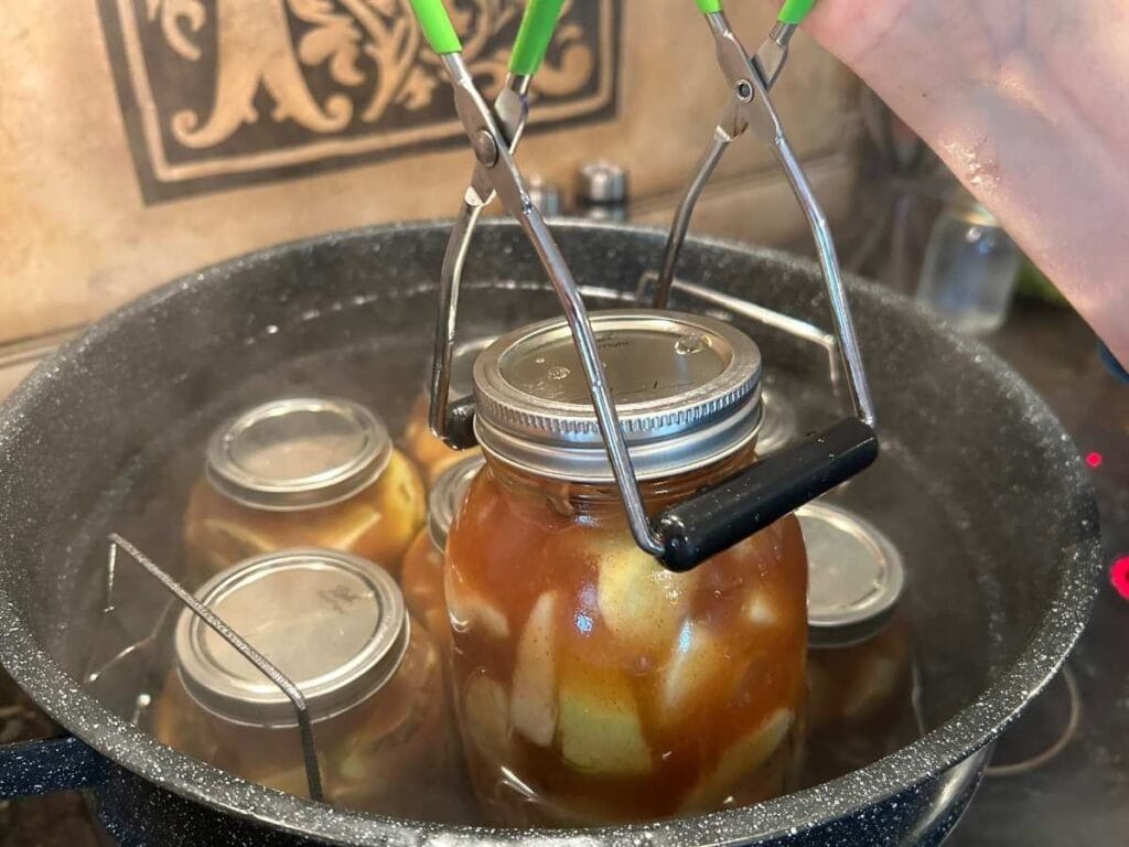 lowering canning jars into the water bath canner with the lifter tool