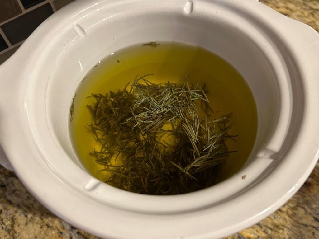 rosemary infusing in tallow in a white crock pot